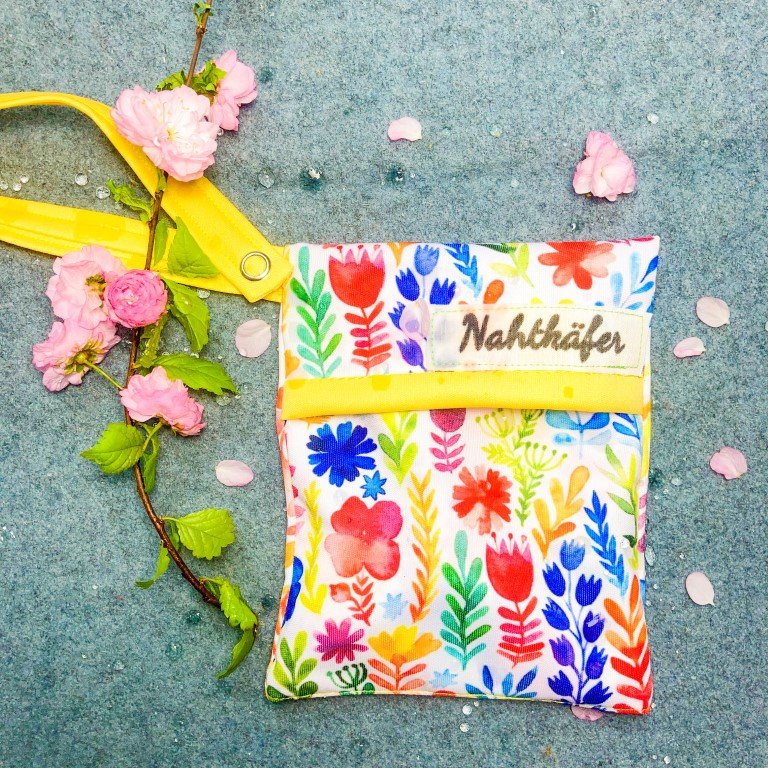 Nahtkäfer Mini Wetbag im Blumen Design auf grauem Wolluntergrund, dekoriert mit rosa Blüten
