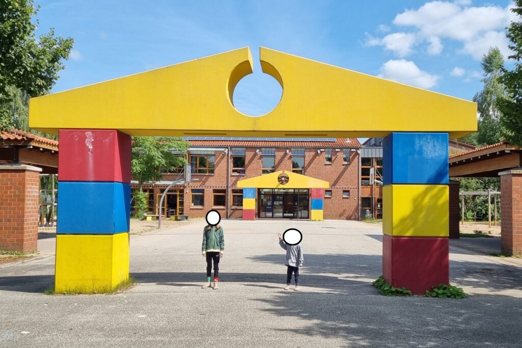 Die Kinder stehen unter einem großen Bogen, der aussieht wie bunte Spielbauklötze.